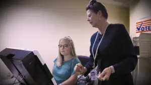 person with disability using an accessible voting machine. a poll worker guides them through the process